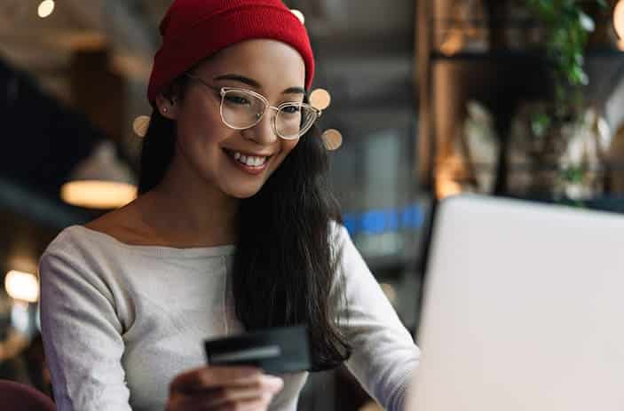Young smiling women with spectacles holding a credit card and making an online payment through her laptop