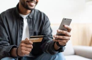 Smiling man holding a credit card in his hand and making an online payment through his phone